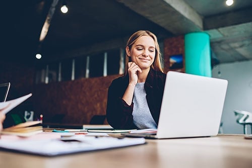 The woman looks at the laptop screen with a smile.