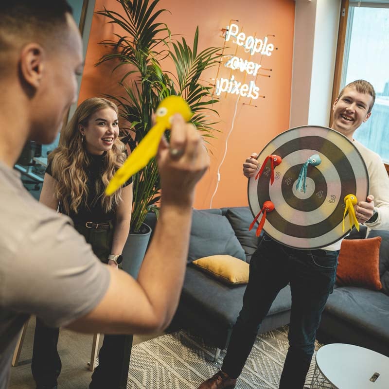 Workers in the break room throwing darts.