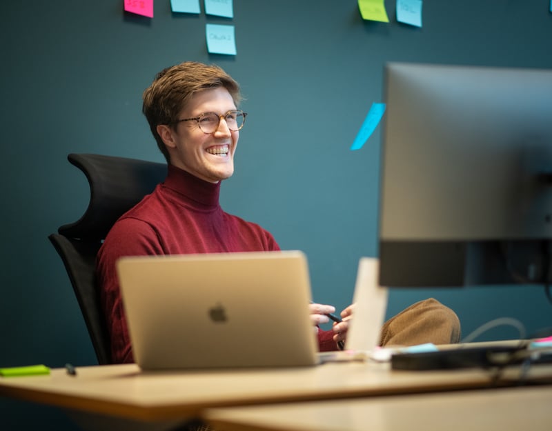 Mann sitter bak to PC-skjermer og smiler
